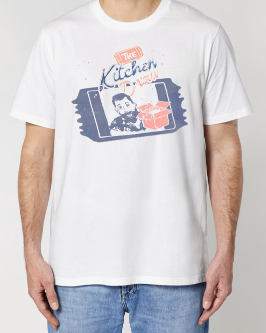 A man wearing a white short-sleeve t-shirt with a colourful graphic print on the front that reads 'The Kitchen Draw' and features a stylised portrait, set against a plain light grey background.